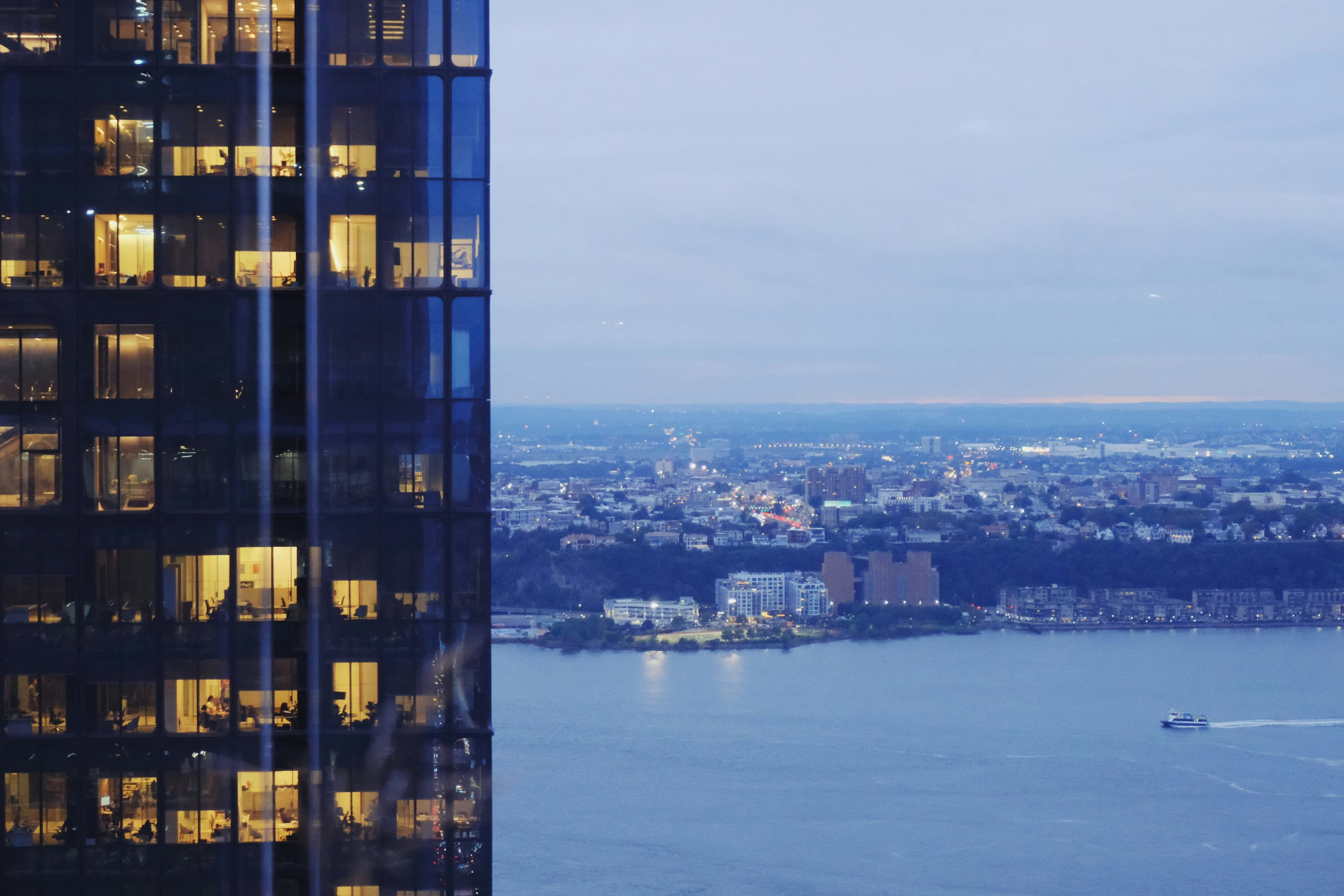 A glass office tower at dusk overlooking the river and city skyline